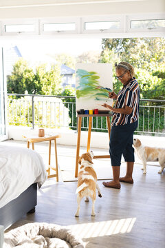 African American senior woman painting on canvas at home, dogs nearby