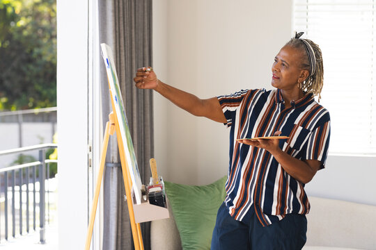 A senior African American woman is painting on canvas at home