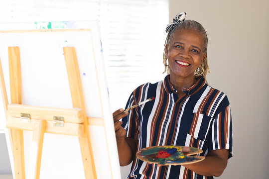 African American senior woman painting on canvas at home, wearing striped shirt