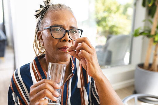 Fototapeta A senior African American woman wearing glasses taking medicine at home