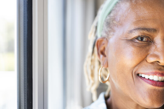 A senior African American woman with a bright smile standing by a window at home, copy space