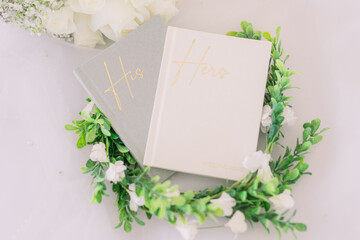 A lay flat of his and her wedding vow books from a bride and groom surrounded by a green and rose...