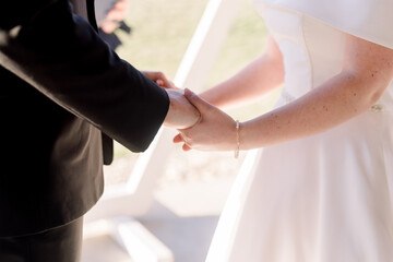 A bride and groom are holding hands during their wedding ceremony