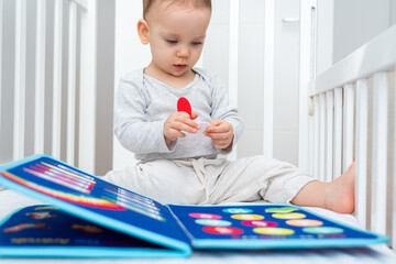 Little baby girl playing with busy book while sitting in crib. Concept of quiet books and modern educational toys