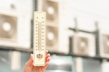 Hot temperature, Hand holding thermometer with blurred air conditioner compressor