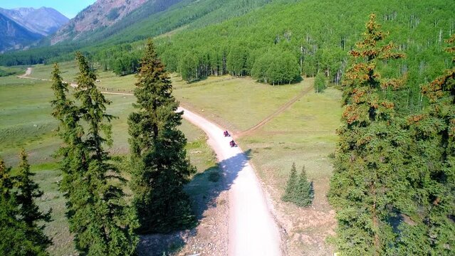 Aerial Backward Ascending Shot Of People Driving Off-Road Vehicles In Forest Amidst Tranquil Mountains On Sunny Day - San Juan Mountains, Colorado