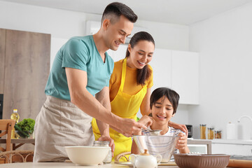 Happy parents with their little son preparing dough in kitchen