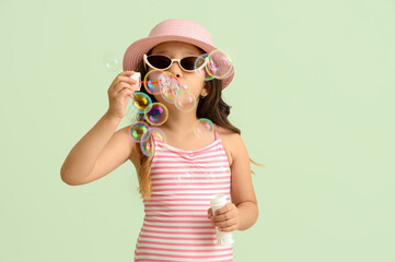 Cute little girl blowing soap bubbles on green background