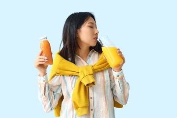 Beautiful Asian woman with bottles of juice on blue background