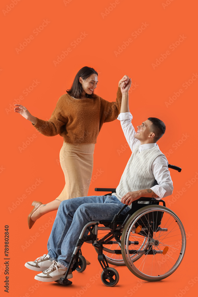 Wall mural Young man in wheelchair and his wife dancing on orange background