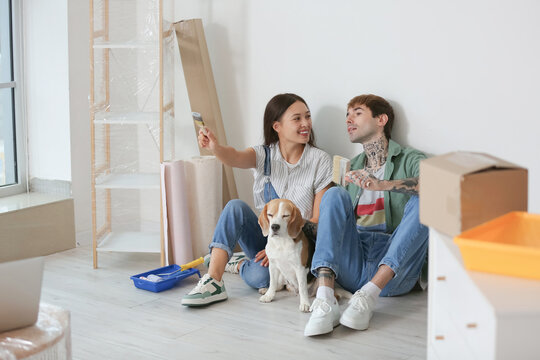 Young couple with paint brushes and Beagle dog sitting during repair in their new house