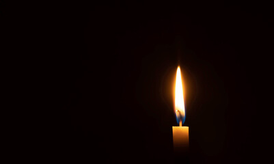A single burning candle flame or light glowing on small orange candle on black or dark background...