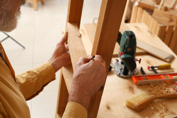 Mature carpenter working with wooden ladder in shop, closeup