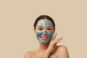 Young woman with clay mask on her face against beige background