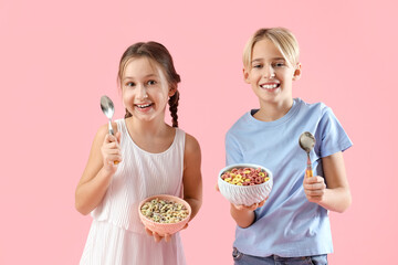 Cute little children with bowls of cereal rings and spoons on pink background