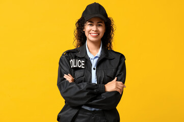 Beautiful young happy African-American policewoman on yellow background