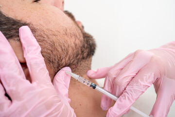 Doctor performing jawline contouring with Botox: cosmetic procedure for male patient's facial...