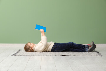 Little girl reading books while lying on floor near green wall
