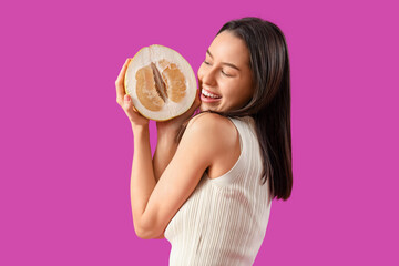 Smiling young woman with half of pomelo on purple background