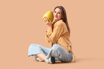 Smiling young woman with pomelo sitting on brown background
