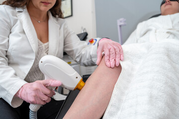 Female doctor performing laser hair removal and epilation procedure on young woman's leg at...