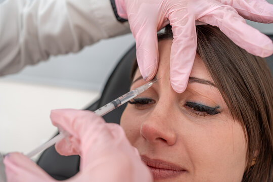 Beautician injecting Botox for eye wrinkle rejuvenation in forehead area, targeting frown lines: skin beautification procedure with botulinum toxin