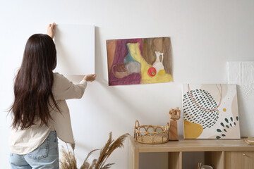 Female Asian artist hanging canvas on wall at home, back view