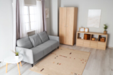 Blurred view of modern living room with grey sofa and wooden closet
