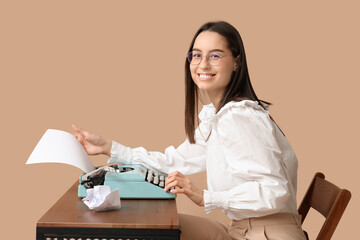 Beautiful young woman with vintage typewriter at table on brown background