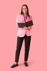 Young female writer with notebook on pink background