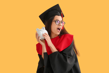 Shocked female graduate with piggy bank on yellow background. Tuition fees concept