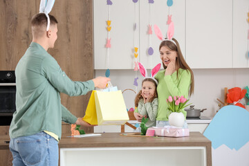 Little girl with her mother receiving gifts from father in kitchen