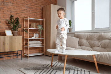 Little boy standing on table at home. Child in danger