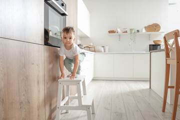 Little boy climbing on step stool near oven in kitchen. Child at risk