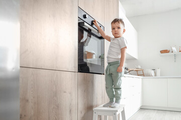 Little boy on step stool opening electric oven in kitchen. Child at risk