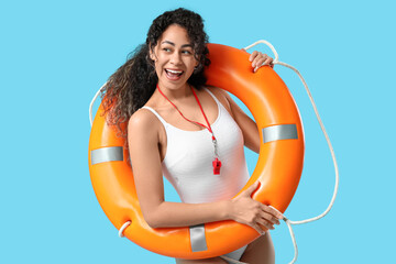 Beautiful young happy African-American female lifeguard with ring buoy on blue background