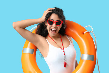 Beautiful young happy African-American female lifeguard with ring buoy on blue background