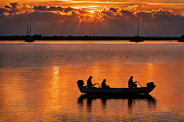 A silhouette of a boat with four people on it, on a calm sea with a golden sunset in the background.