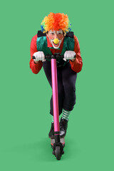 Portrait of clown riding kick scooter on green background. April Fool's day celebration