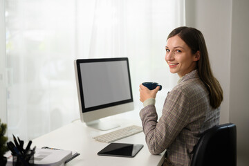Fototapeta na wymiar Millennial businesswoman drinking hot coffee while working online from home office