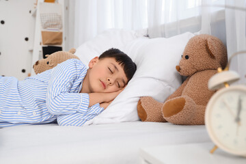 Cute little boy with alarm clock and toys sleeping in bedroom