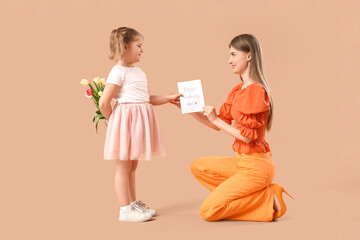 Little girl greeting her mom with Mothers Day with bouquet of tulips and greeting card on beige background