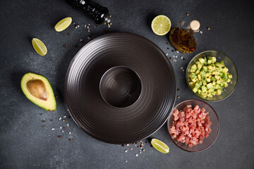 Tuna and avocado tartare recipe - sliced chopped ingredients and form on a dark table