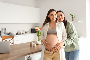 Young lesbian woman hugging her pregnant wife in kitchen