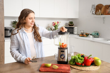 Beautiful young woman with blender making smoothie in kitchen