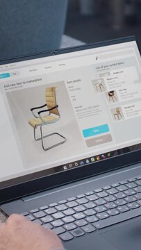Craftsman uploads pictures of stylish wooden chair to online store using laptop computer. Small business owner adds photos of handmade products to the marketplace for sale. Vertical shot