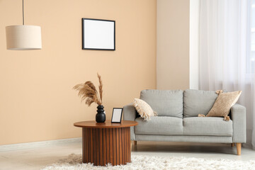 Stylish living room with sofa and blank picture frame on beige wall