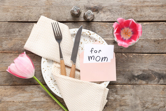 Table setting with greeting card for Mother's day and tulip on wooden background