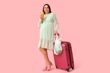 Young pregnant woman with suitcase and cocktail on pink background. Travel concept