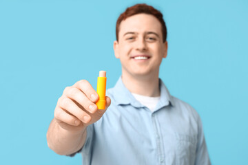 Happy young man with lip balm on blue background